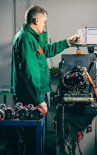 Technician in green work jacket working at a station with multiple turbochargers, performing diagnostics or repair at a workshop table